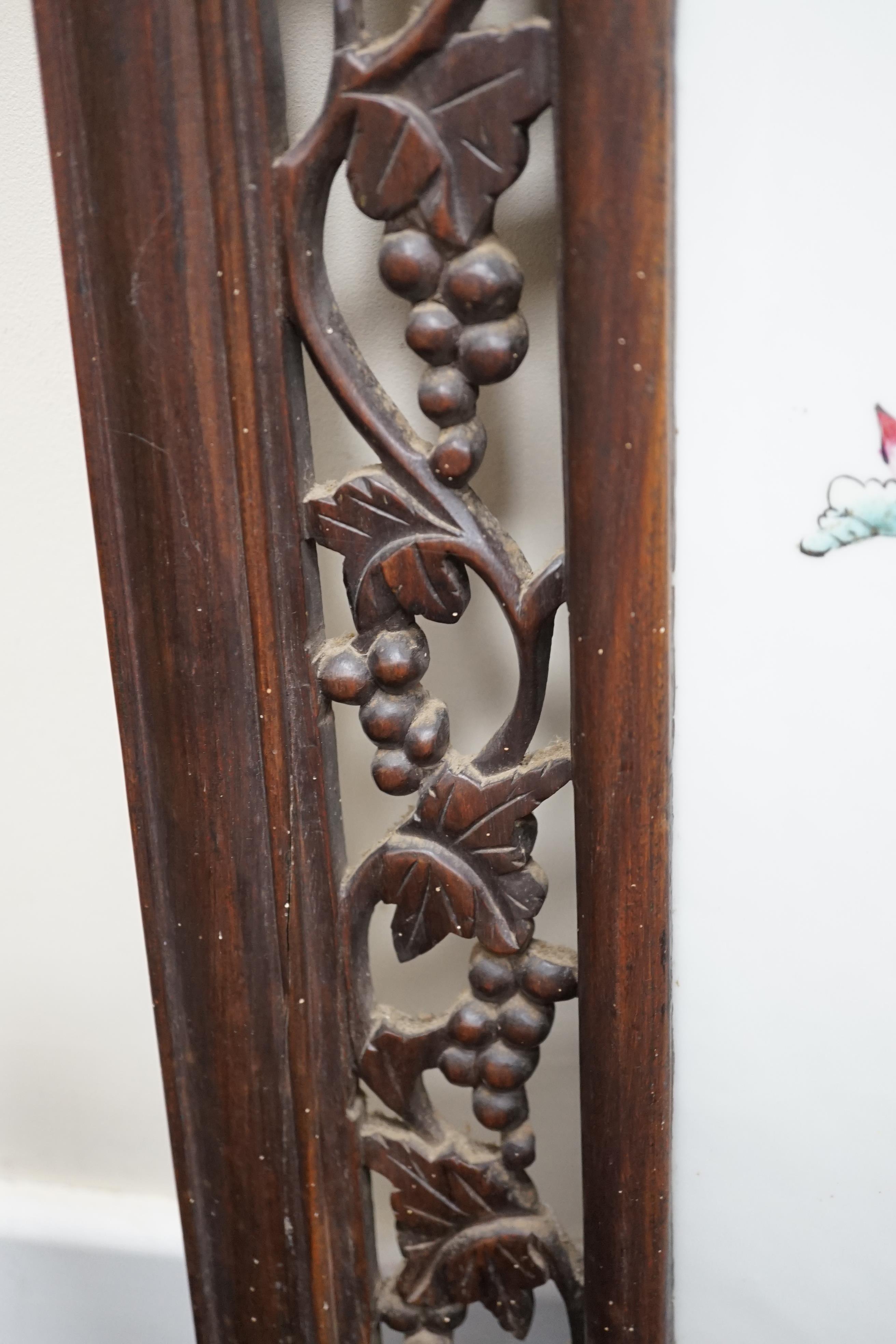 A Chinese enamelled porcelain and hardwood table screen, Republic period, painted with the HeHe Erxian, holding a sprig of lotus and a box and cover, the plaque 37.5cm x 24cm, the wood stand and frame carved with vines,